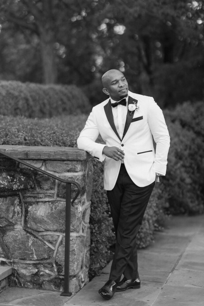 Groom leaning against fence in white tuxedo before Montalto wedding