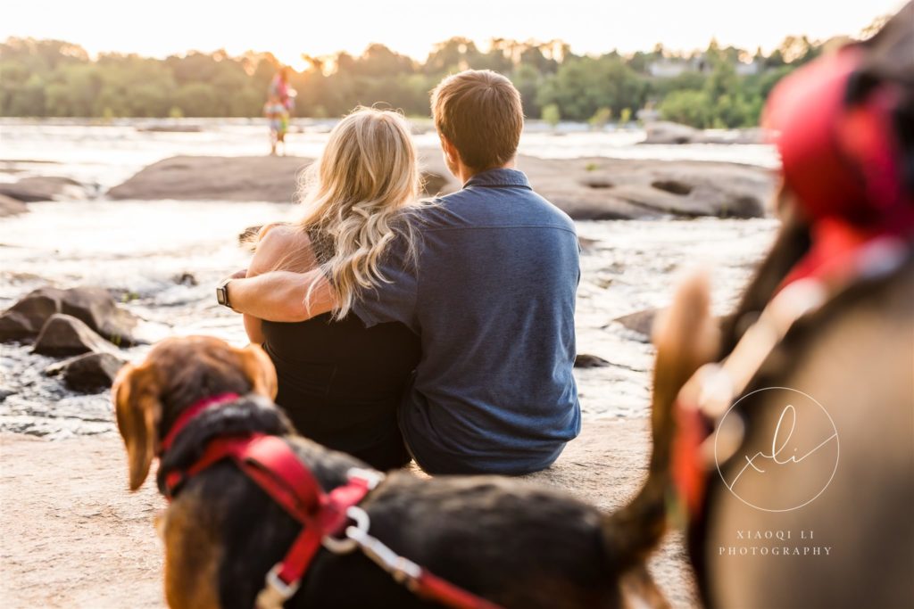 man and woman sitting by waterfront with pups enjoying sunset at Belle Isle