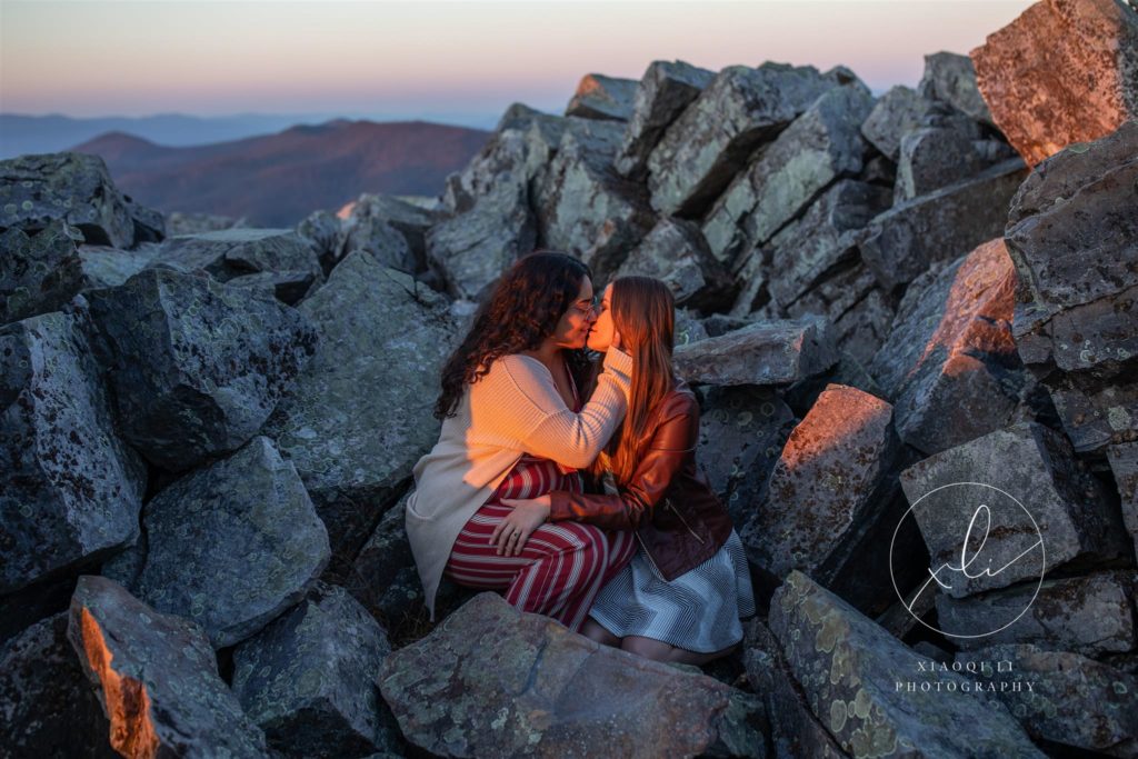 Engaged couple sitting on rocks kissing celebrating together
