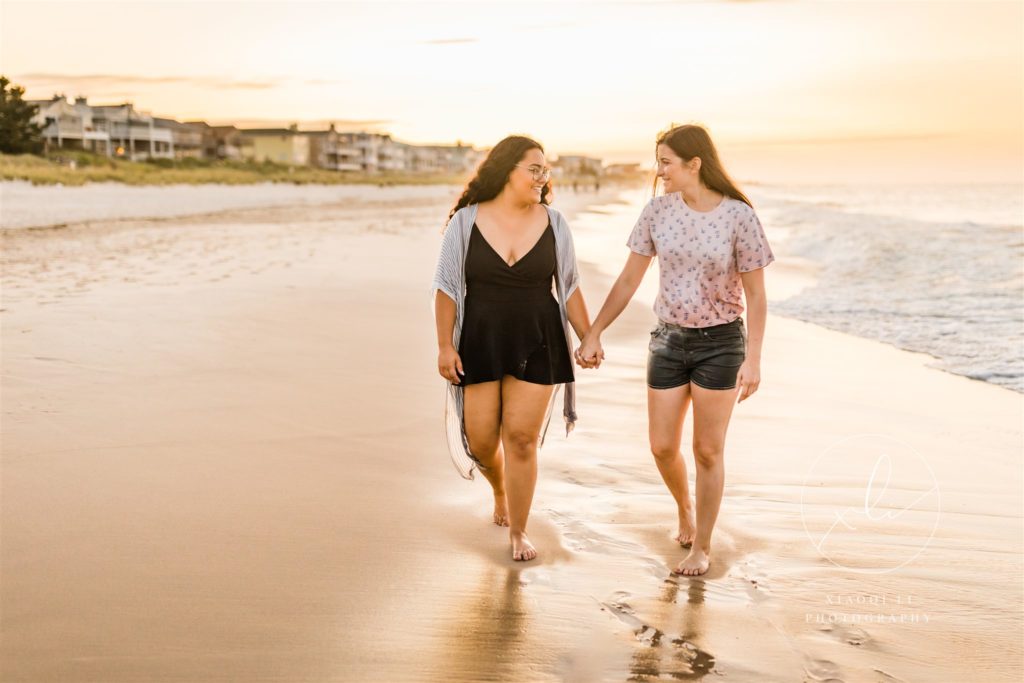 Emily and Sophie walking hand in hand during outdoor engagement session on the beach