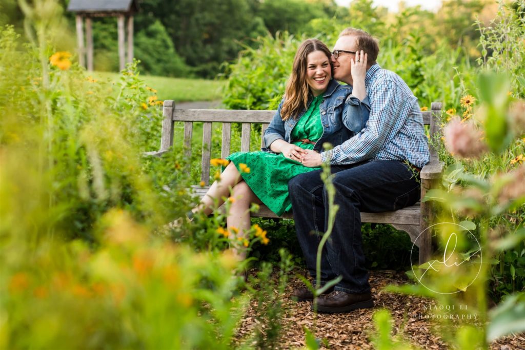 man and woman sitting on bench together laughing and smiling at ivy creek natural area engagement session
