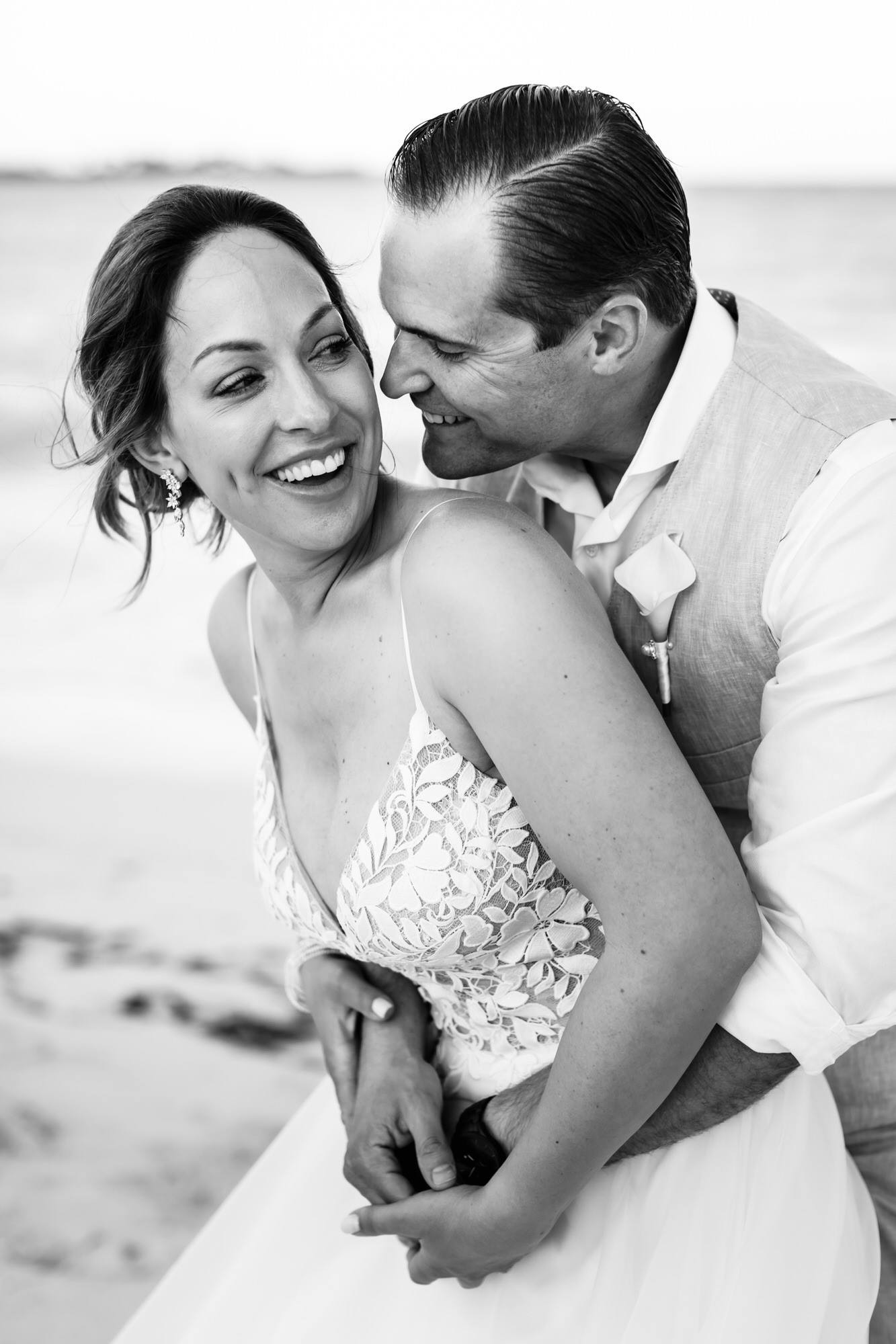 Bride and groom laughing together on beach