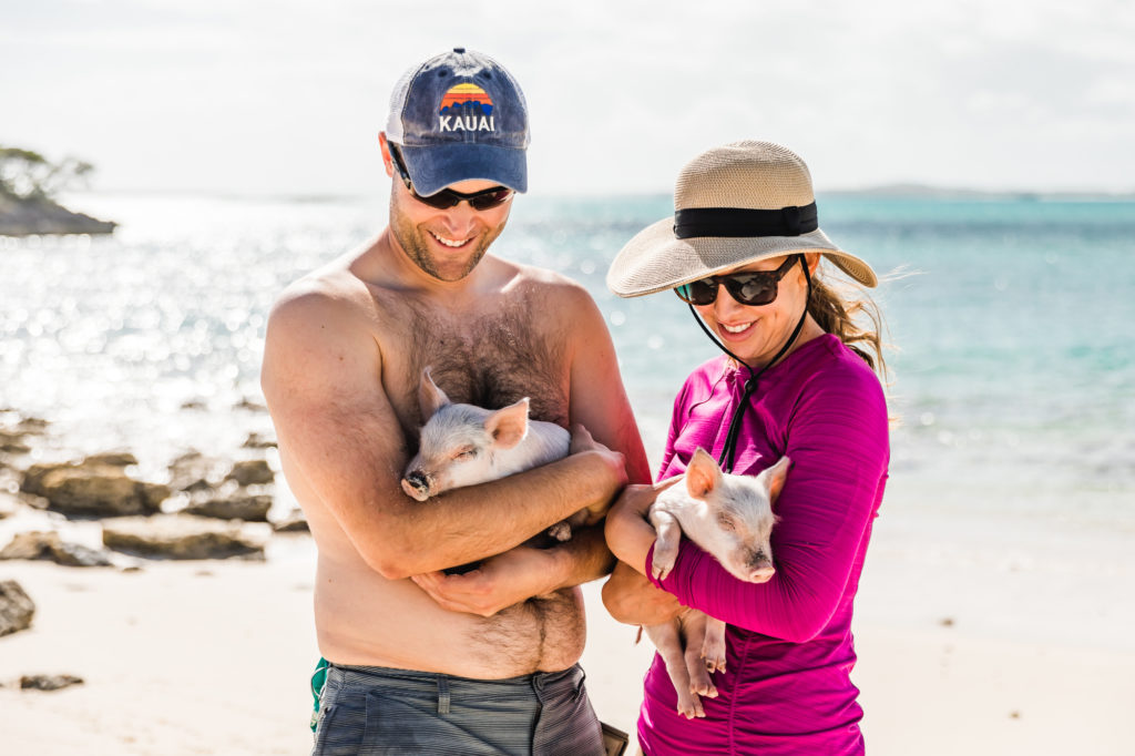 couple holding pigs together on exuma beach coast