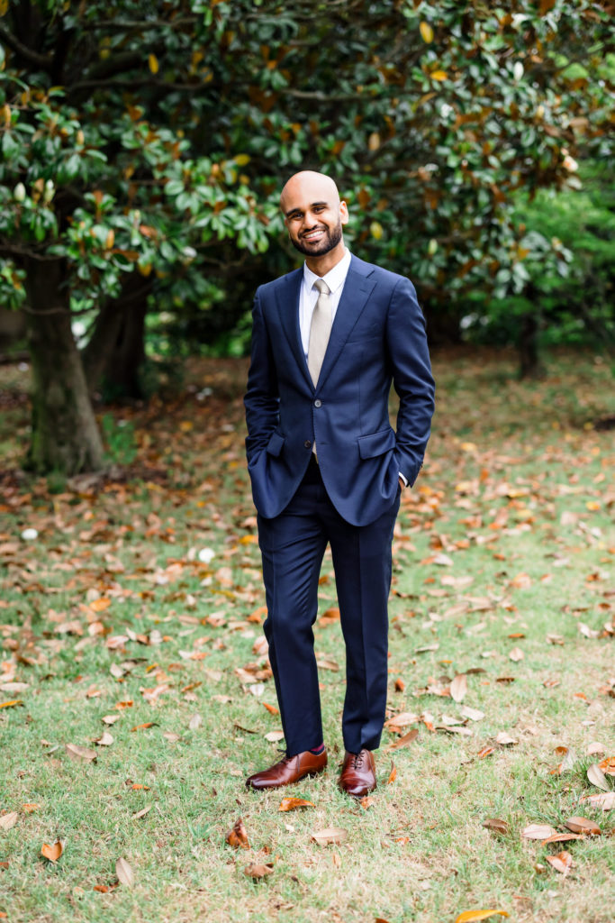groom standing and smiling in navy suit on hindu muslim interfaith wedding day