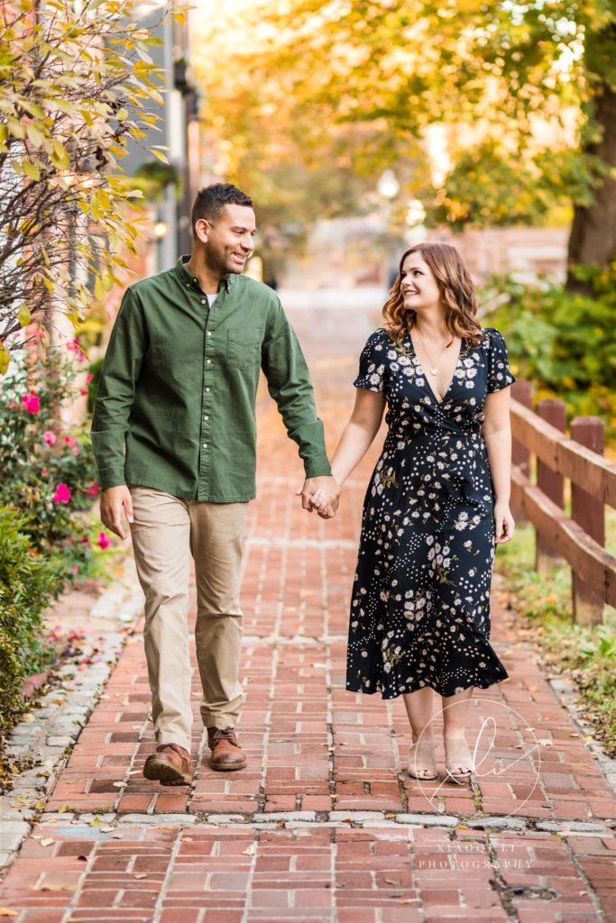 man and woman holding hands and walking throughout Georgetown during fall engagement session
