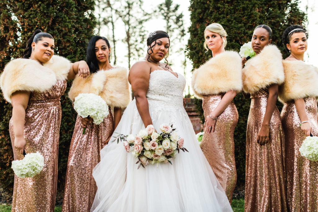 bride posing with bridesmaids wearing sparkly rose gold gowns and fur coverlet during New Year's Eve wedding event