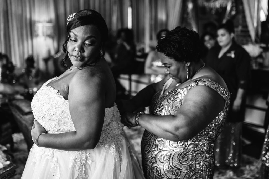 black and white image of bride getting dress on with help of mother on wedding day