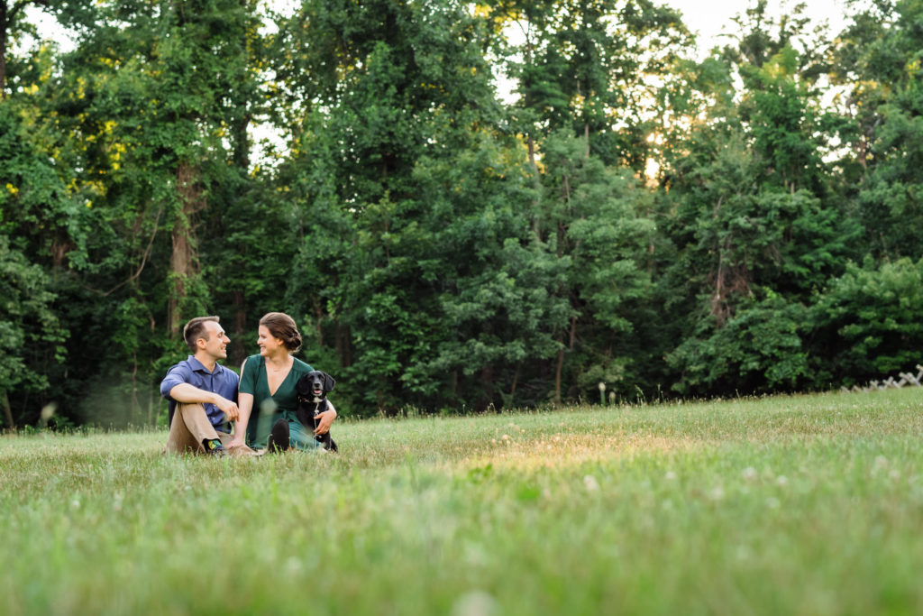 engaged couple sitting on grass in forest area during outdoor engagement session