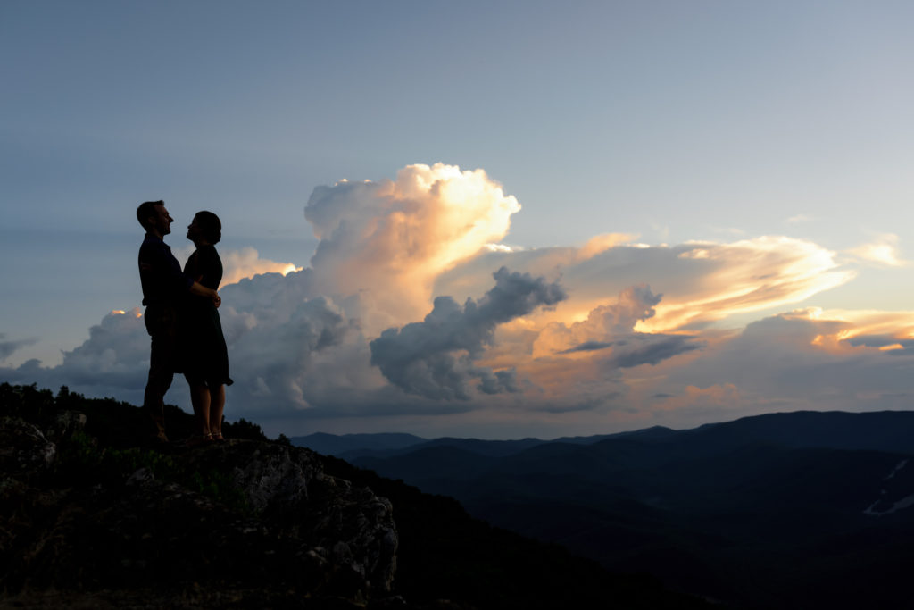 engaged couple embracing at sunset on top of rocky mountains in Charlottesville