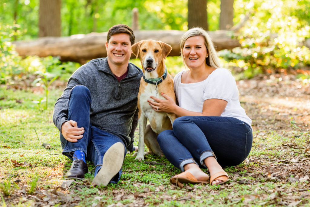 engaged couple sitting with dog and smiling during outdoor engagement session