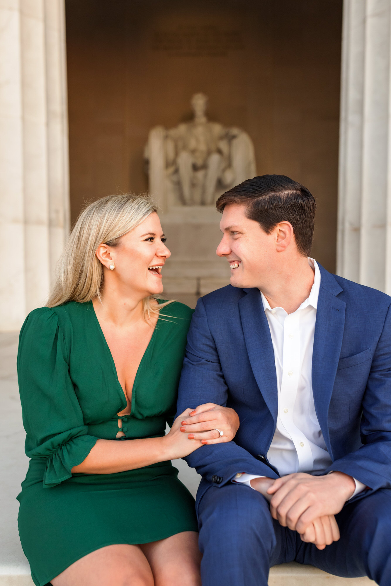 man and woman sitting at Lincoln Memorial laughing together during sunrise engagement session