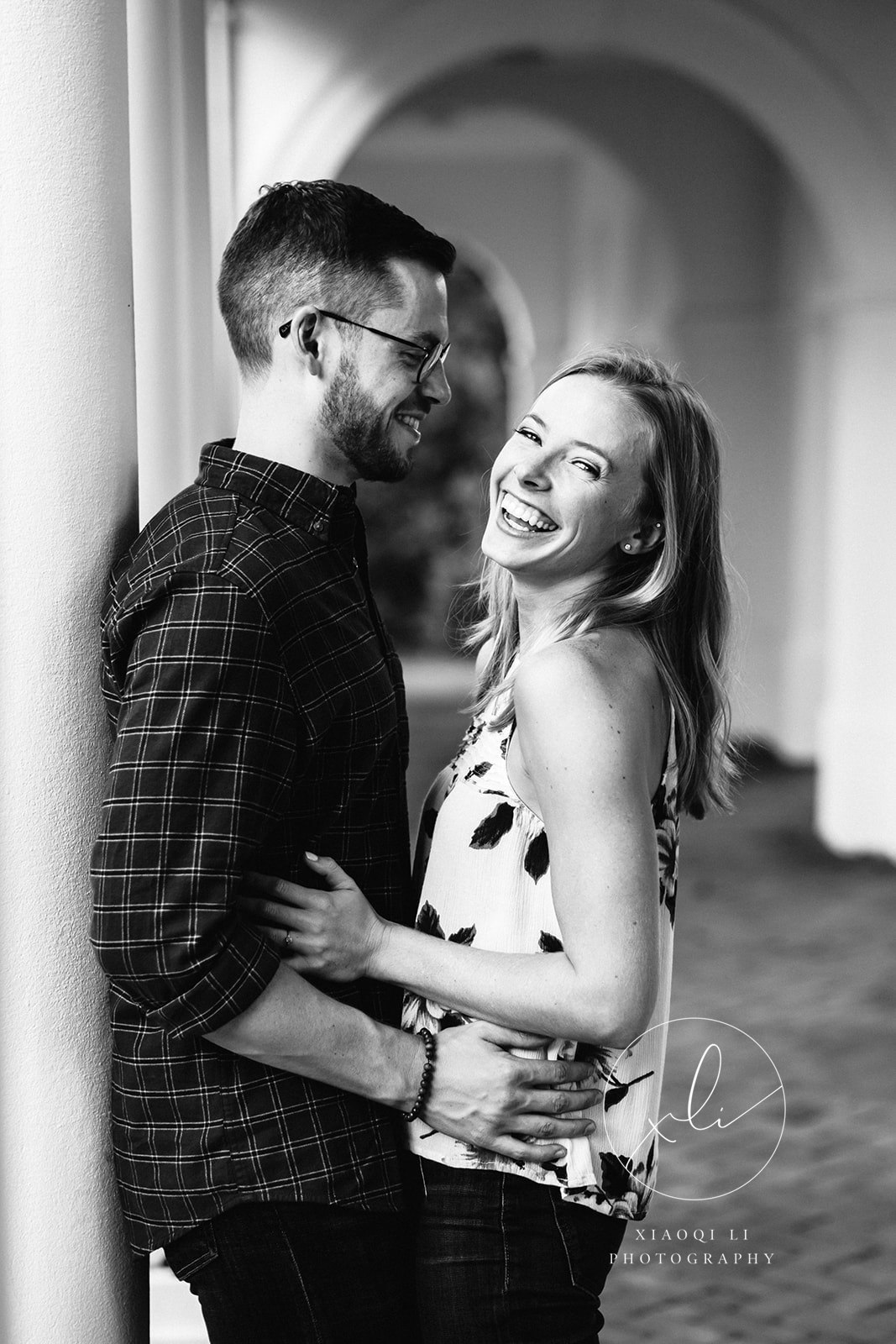 newly engaged couple leaning against wall laughing