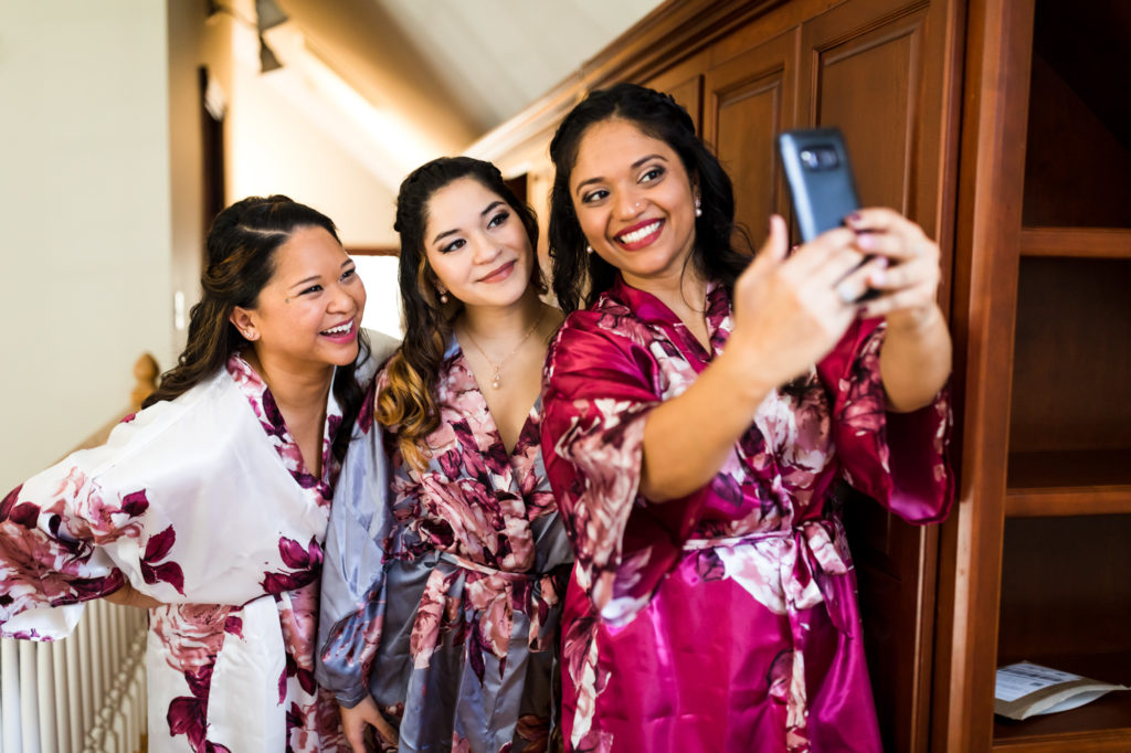 bride taking selfies with bridesmaids in matching floral robes during airbnb wedding