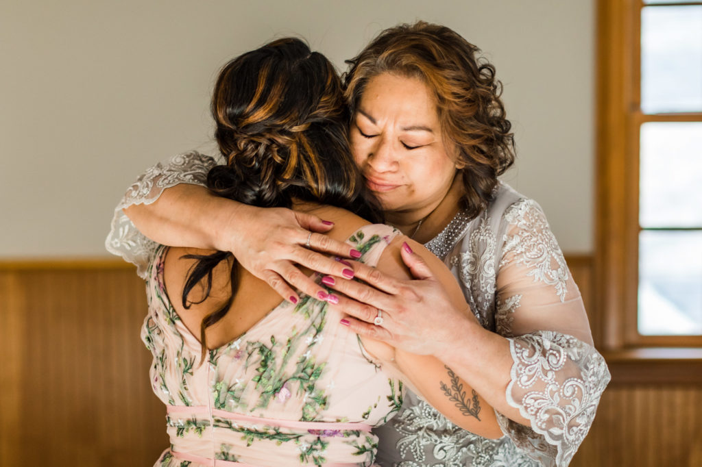mother of bride hugging bride on airbnb wedding day in wedding gowns