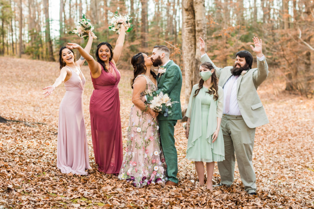 newly married couple kisses while bridal party celebrates and cheers