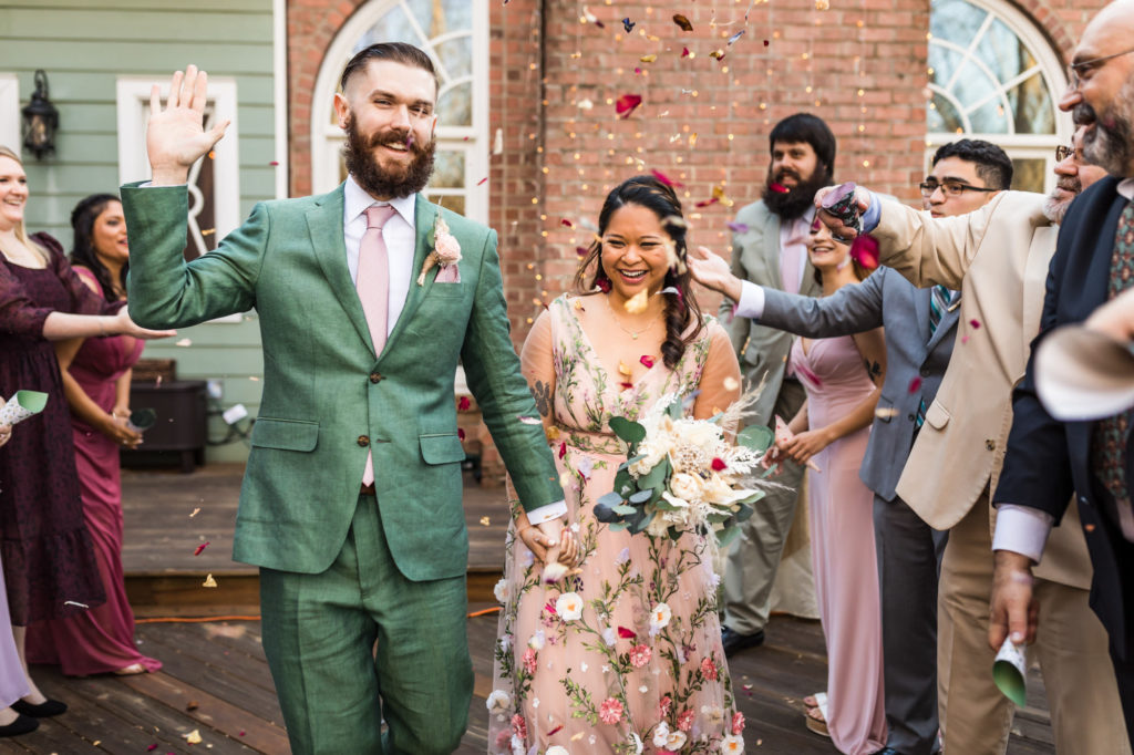 bride and groom walking out together as guests throw flower petals in celebration