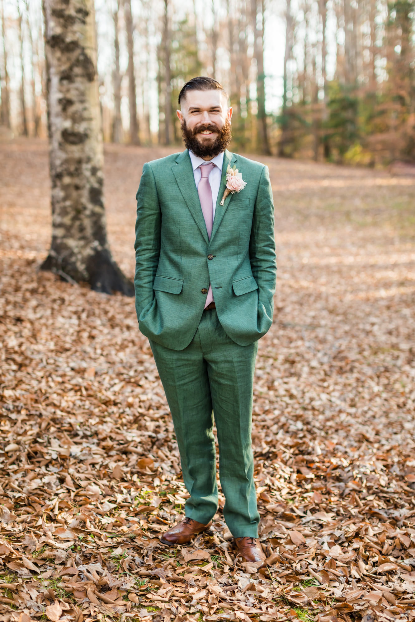 groom smiling in woodland chic wedding bridal portraits wearing green suit and pink tie