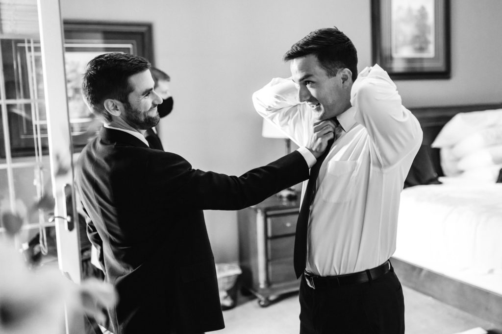 groom getting dressed and putting on tie on wedding day at house mountain inn