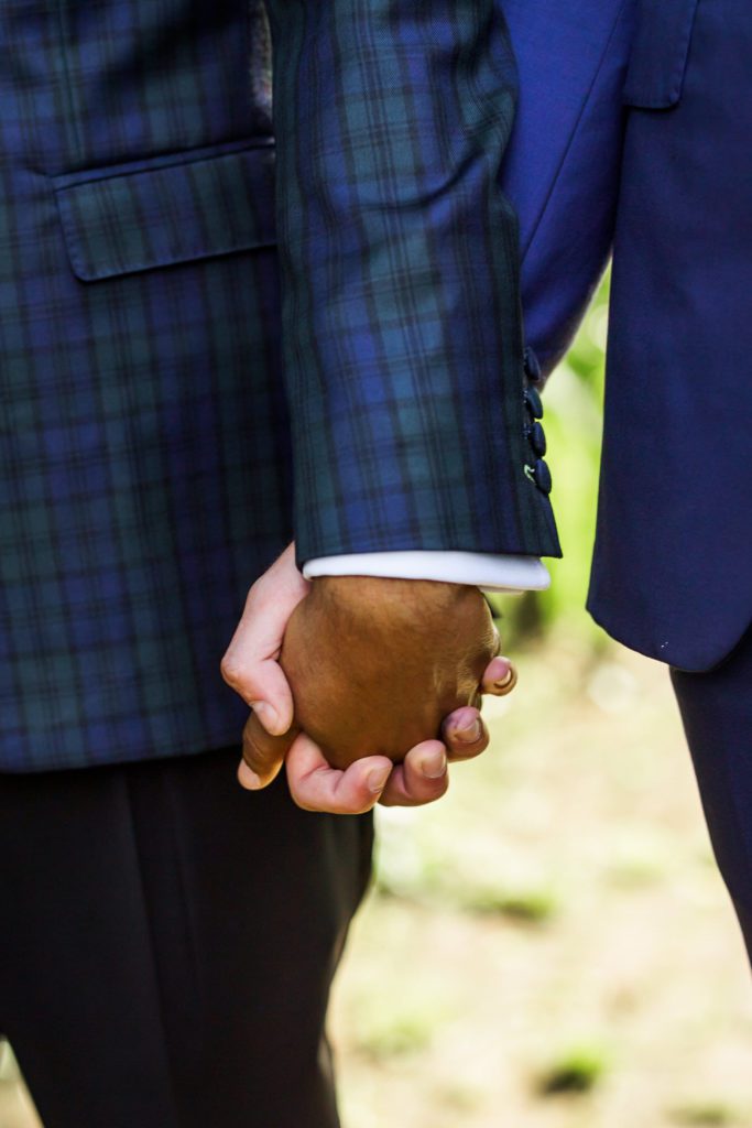 grooms holding hands wearing navy suit and plaid suit