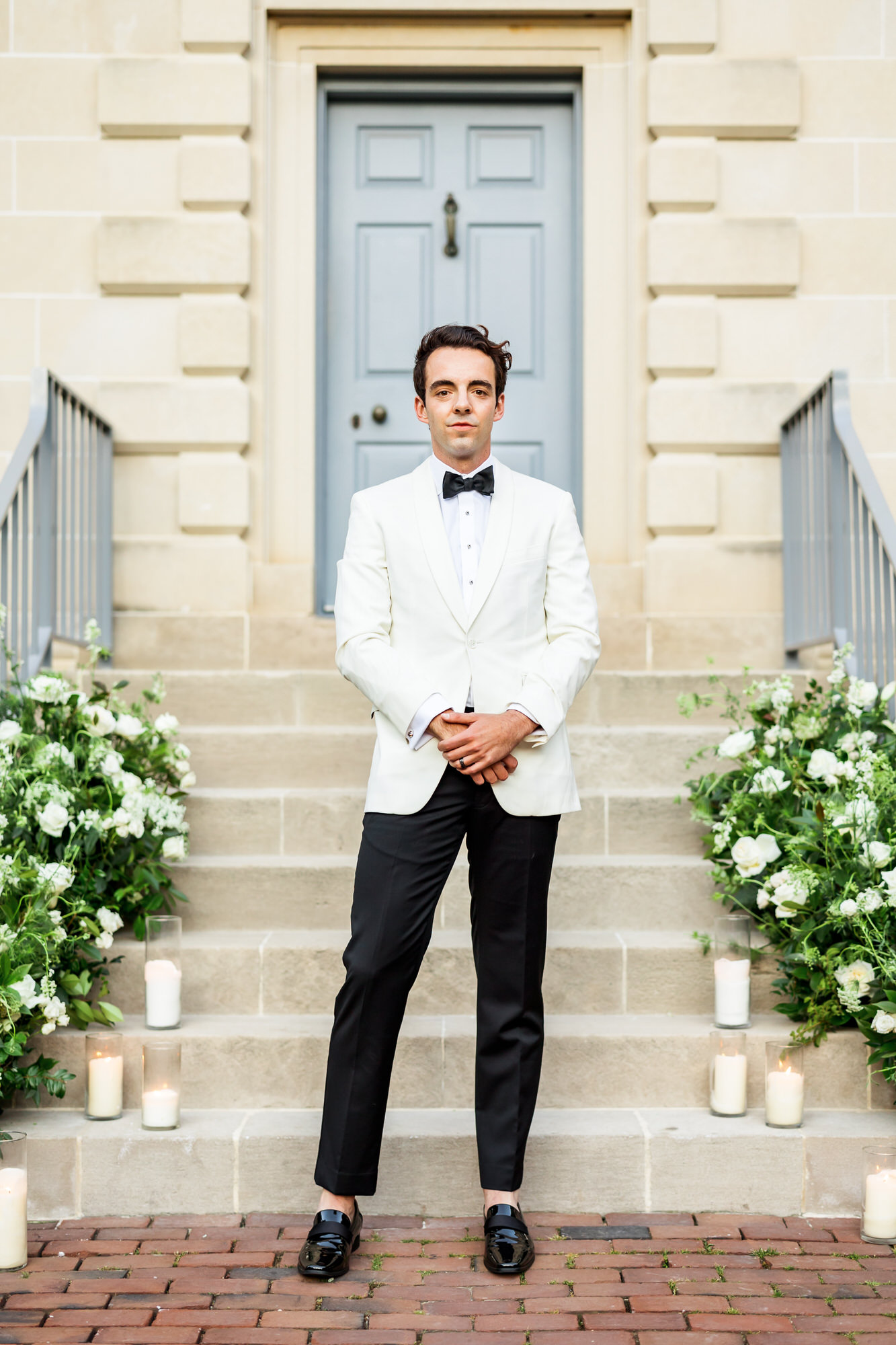 groom wearing white tux jacket with black bow tie at bridgerton spring wedding inspiration