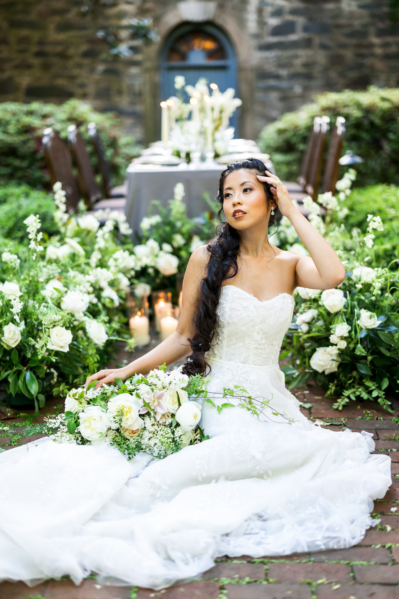 bride with hair in loose braid with white and green bridal bouquet sitting on ground during bridal portraits