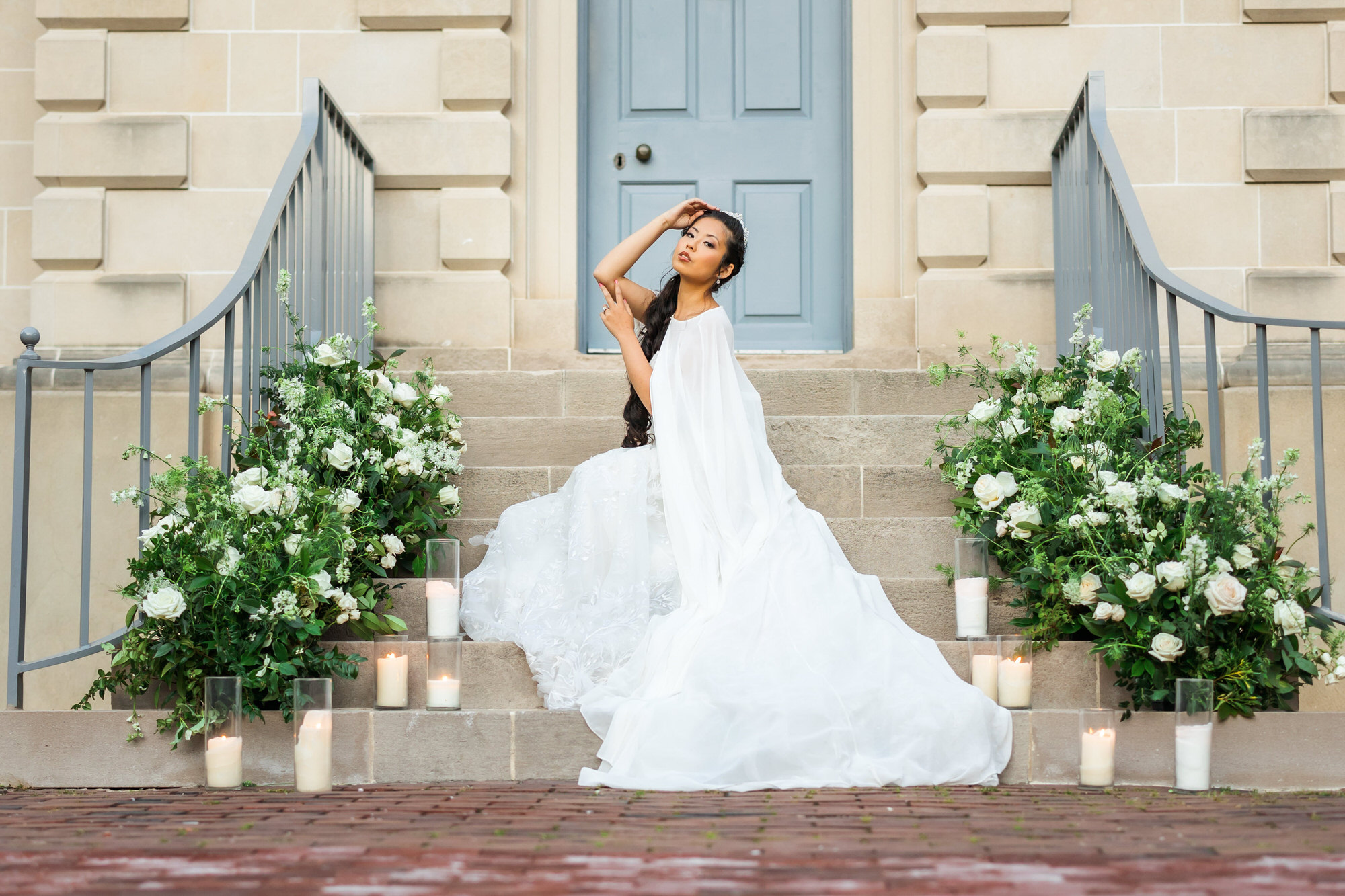 bride sitting on stairs in bridal gown and cape during outdoor bridal portraits