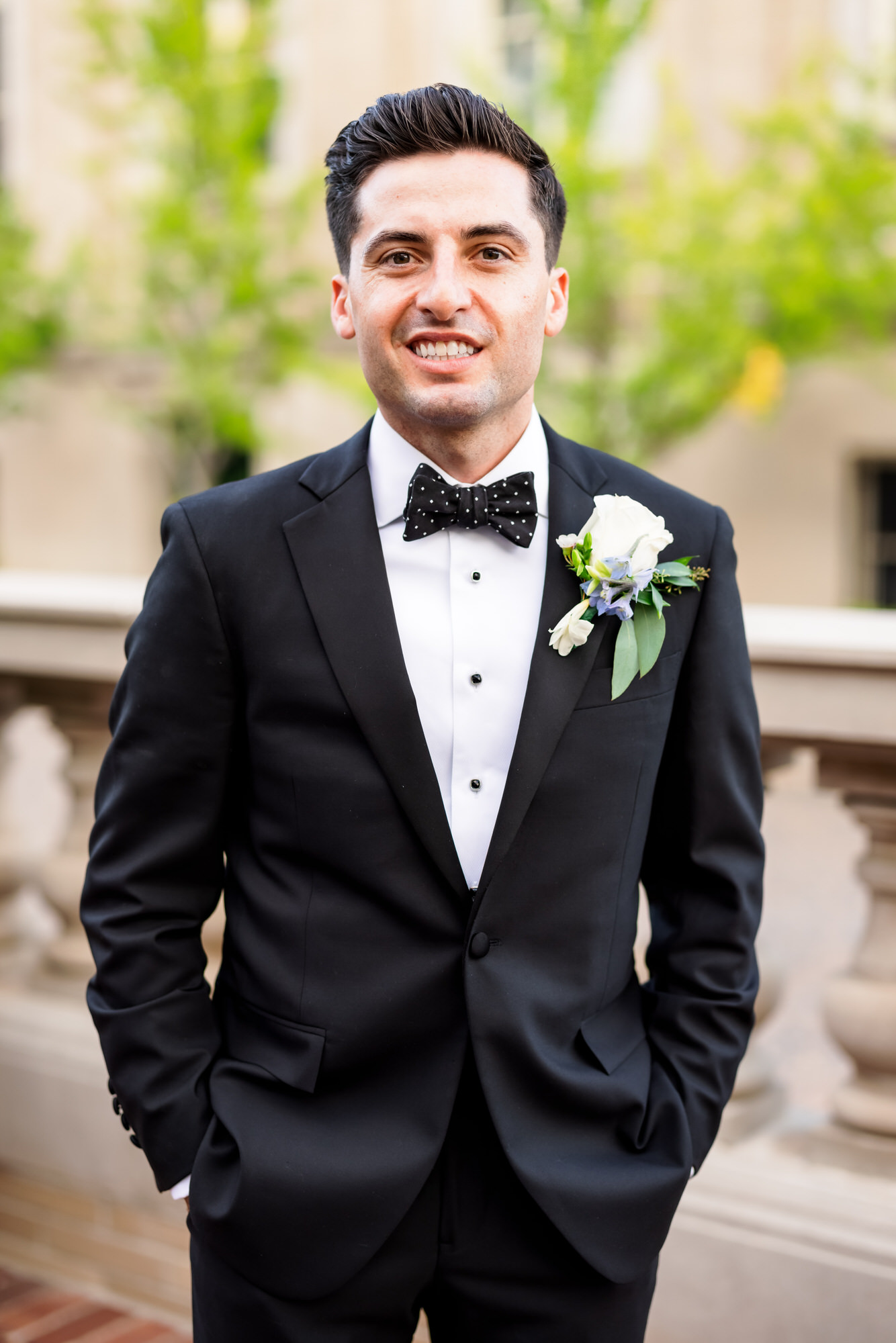 groom wearing tuxedo with hands in pockets smiling
