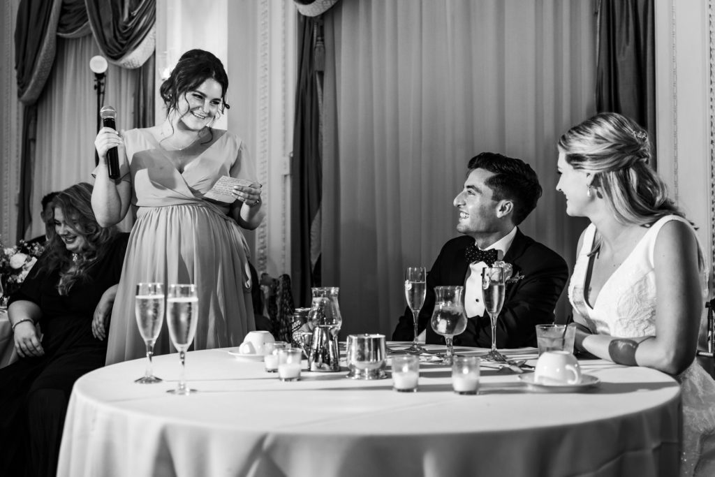 wedding couple sitting at table while bridesmaid gives toast