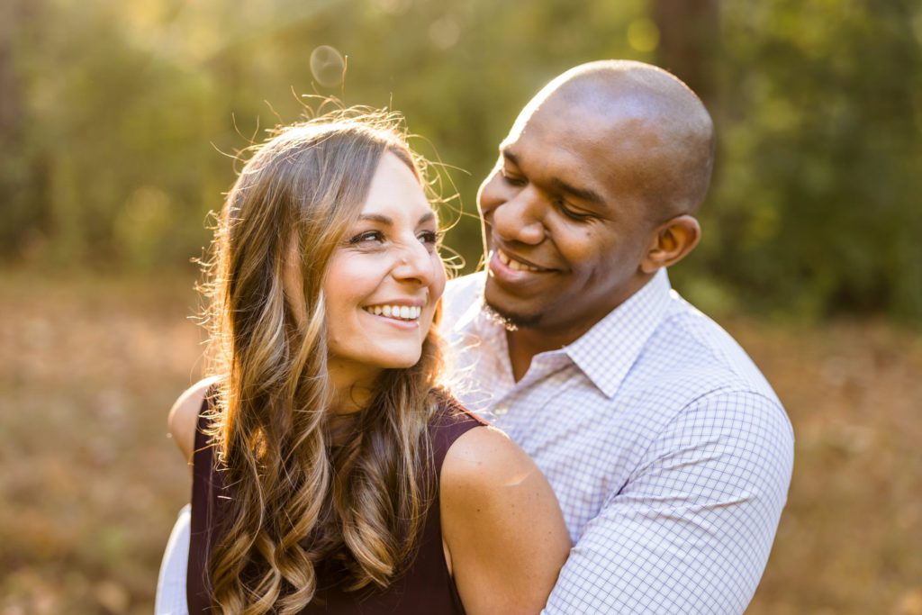 man embracing woman and looking at her smiling while woman looks over shoulder smiling