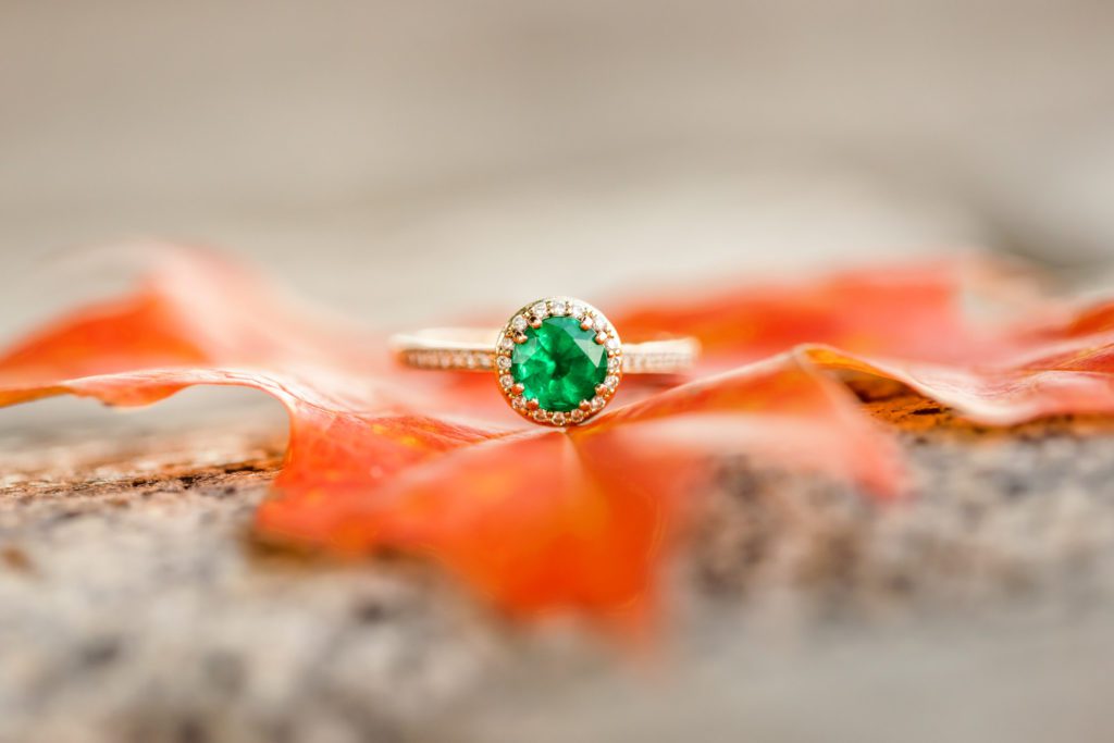 detail shot of emerald engagement ring on orange autumn leaf