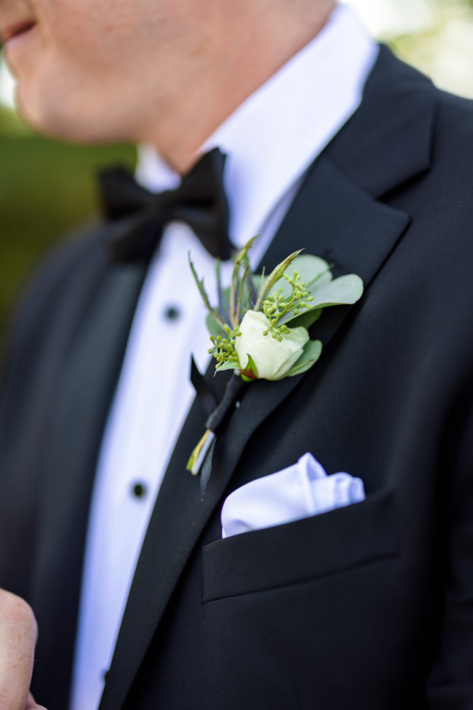 detail shot of boutonniere with green leaves and white flowers 