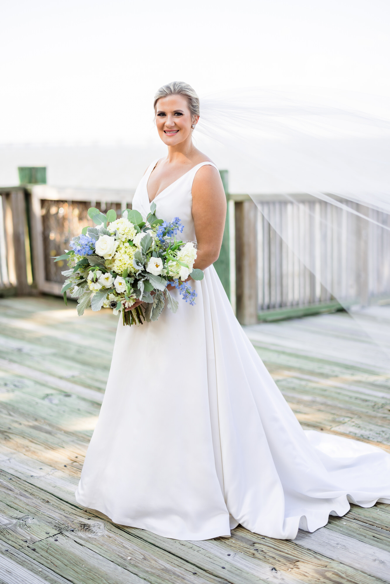 bride holding bridal bouquet with white and green leaves on dock