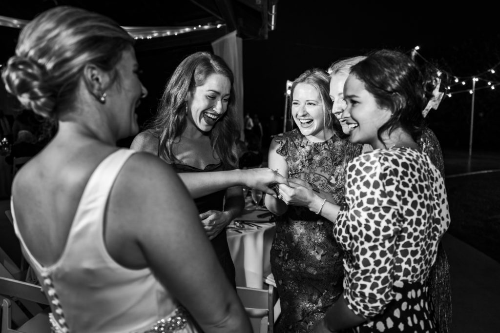 black and white image of guests looking at bride's ring during wedding reception