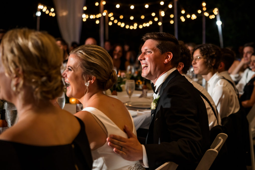 bride and groom laughing during speeches at wedding reception