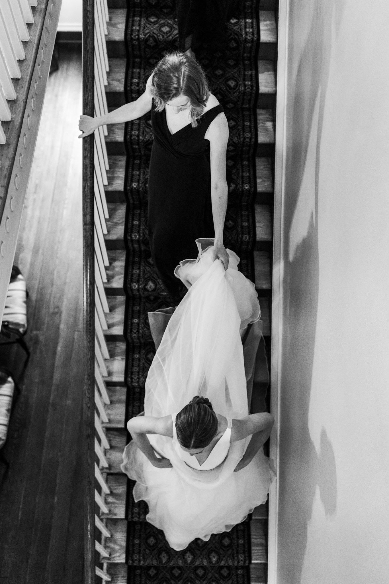 bride walking down stairs wearing bridal gown as bridesmaid holds train