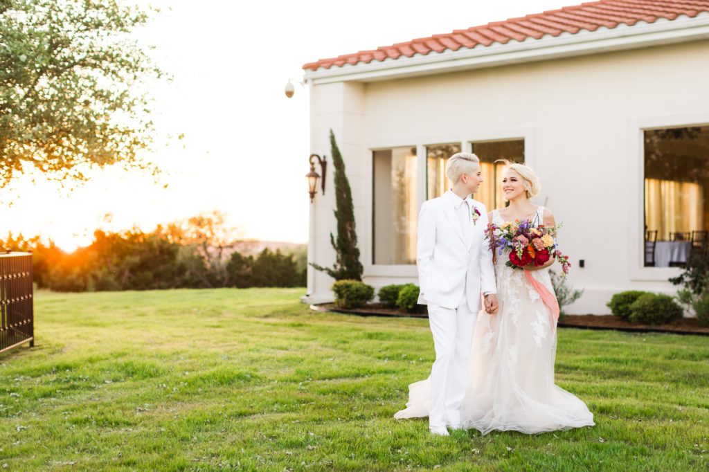 couple walking through grass together with colorful bridal bouquet