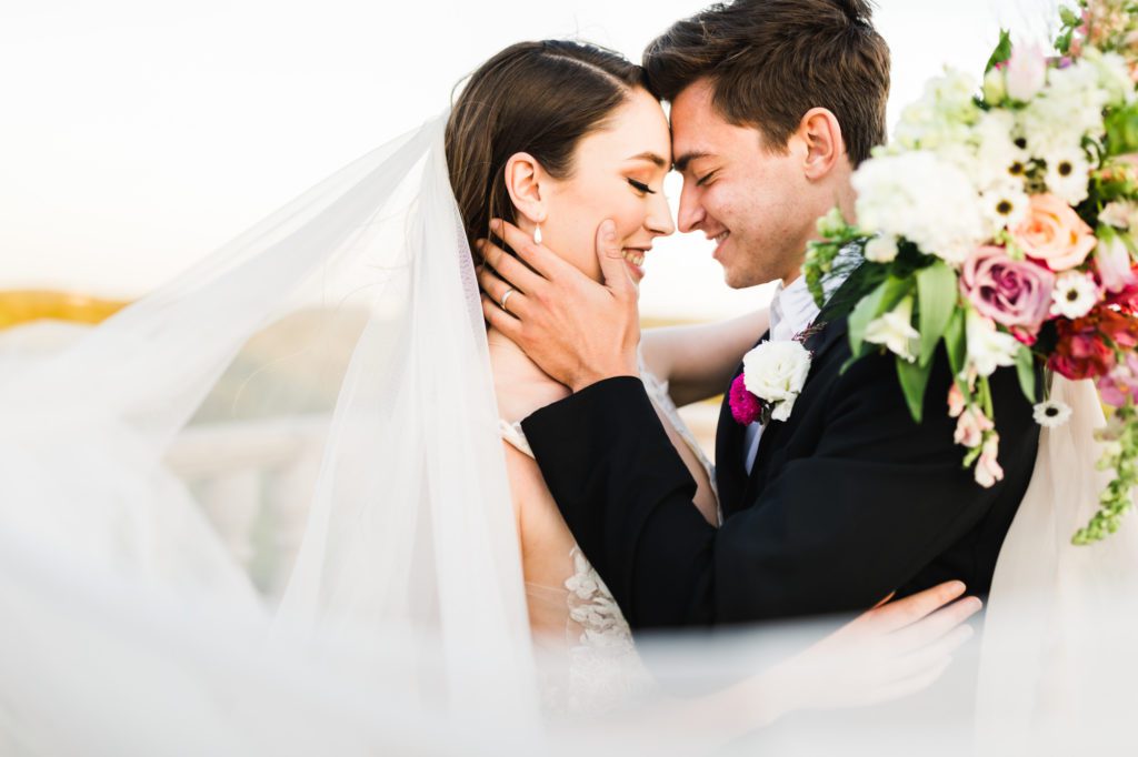 bride and groom embracing with veil and colorful bouquet