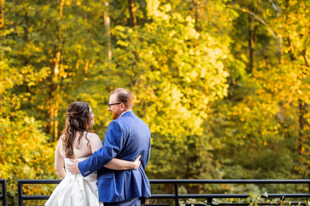 wedding couple embracing looking over Charlottesville's fall leaves