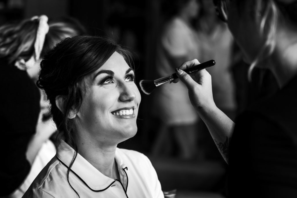 bride getting ready smiling while makeup artist applies makeup in black and white portrait