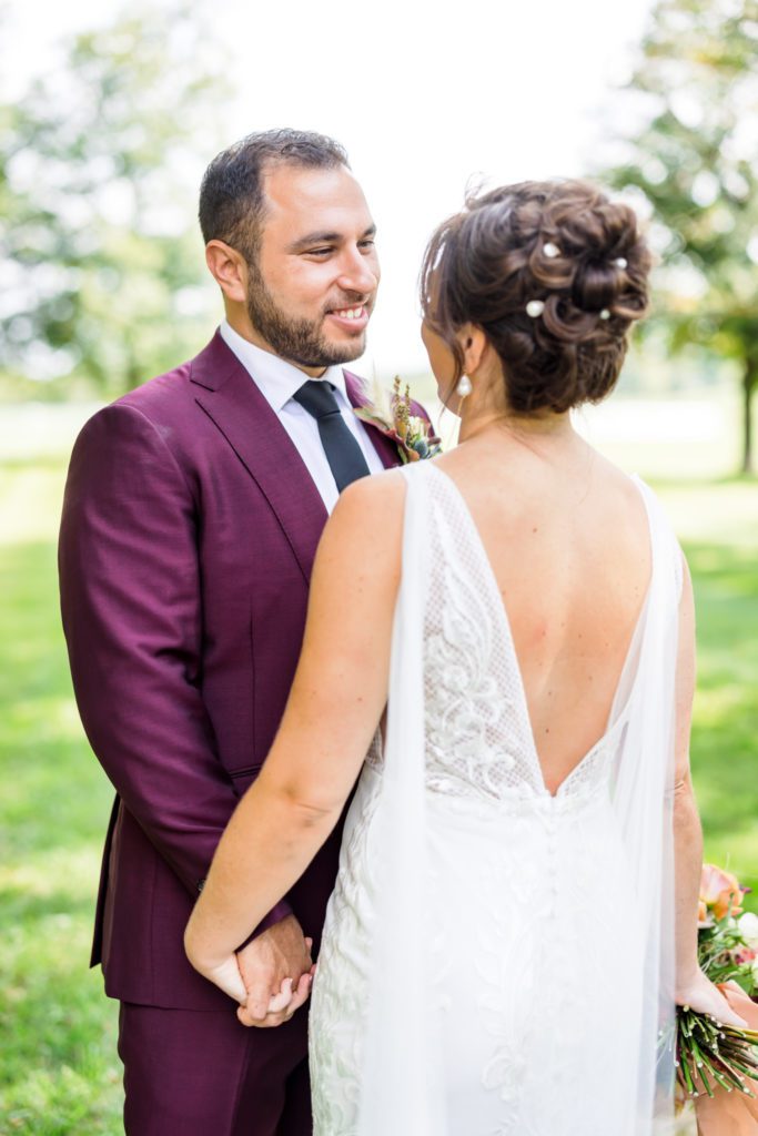 groom smiling at bride during first look while wearing burgundy suit 