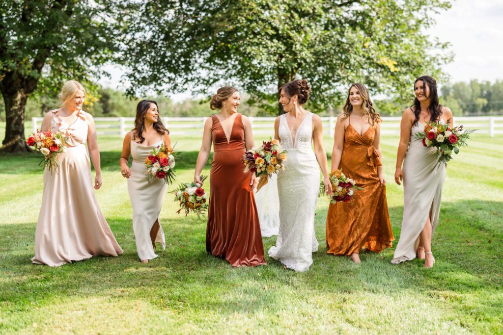 bride walking with bridesmaids wearing rust, orange, and cream bridesmaids gowns