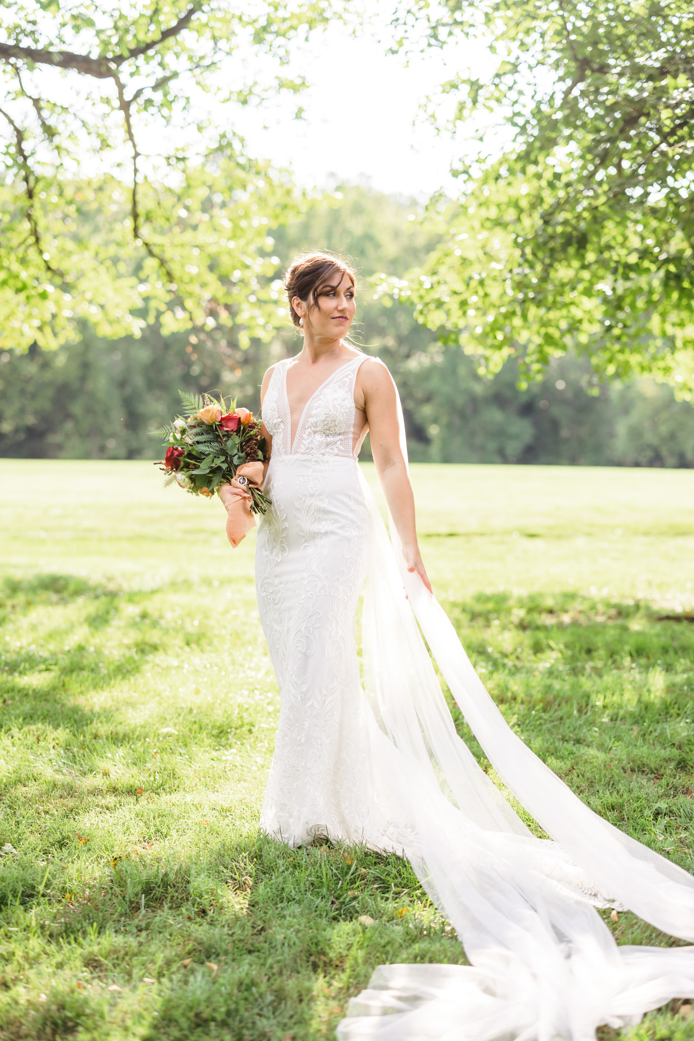 bride wearing ivory lace v-neck wedding gown with cape in green grass during bridal portraits