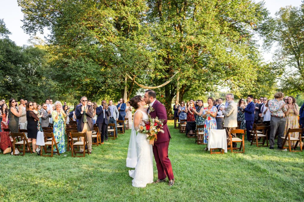 bride and groom walking out of outdoor wedding ceremony and kissing in celebration