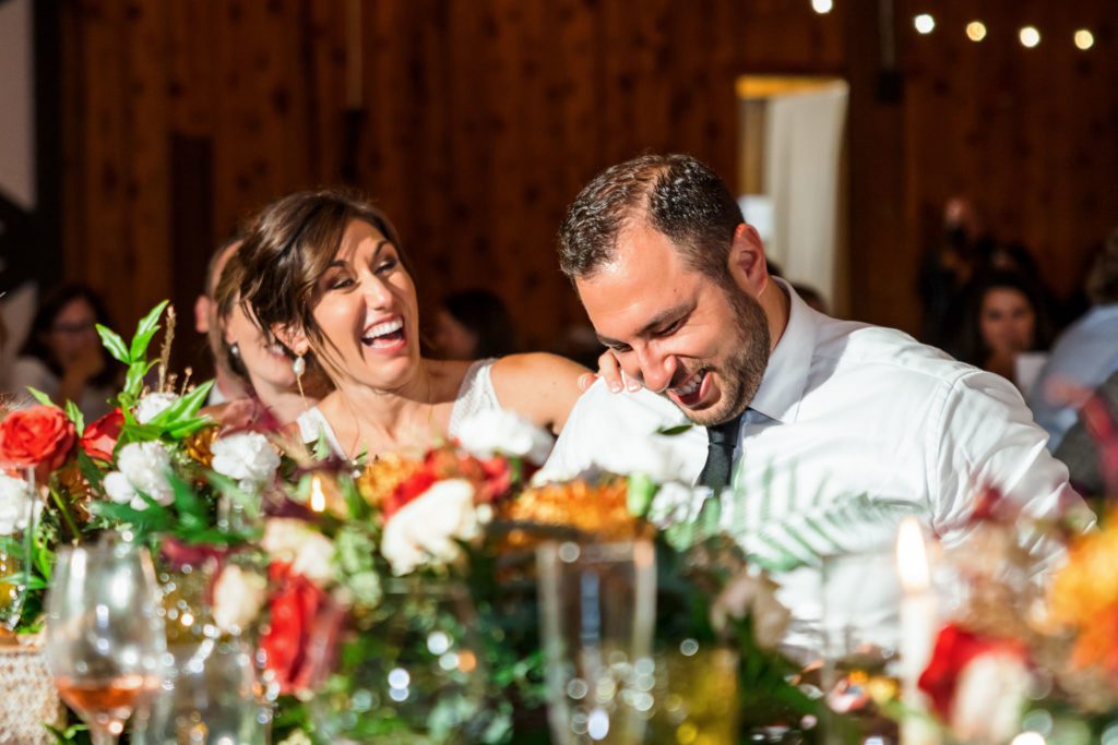 newly married couple laughing during speeches at their Fall Castle Hill Cider wedding