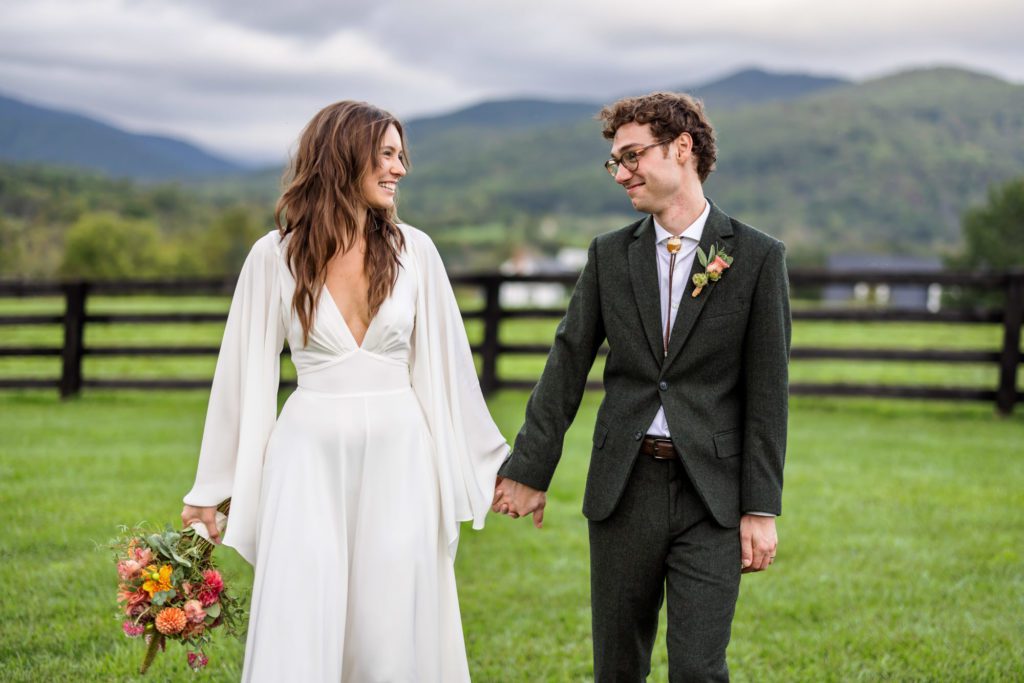 newly married couple walking hand in hand after colorful fall boho wedding