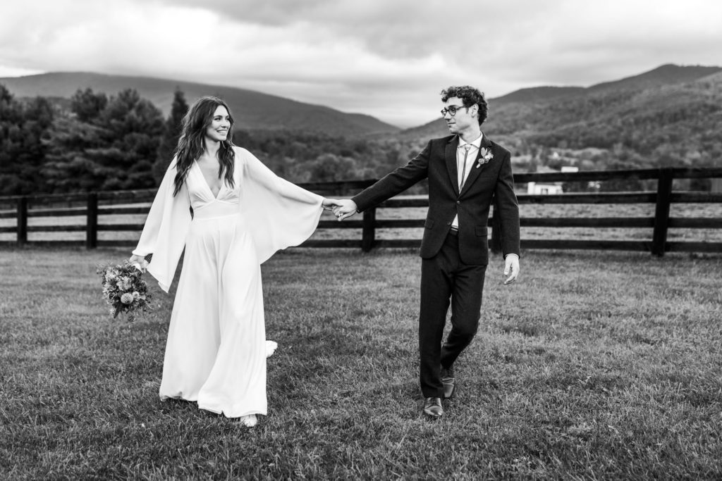 black and white portrait of bridal couple holding hands and walking through field