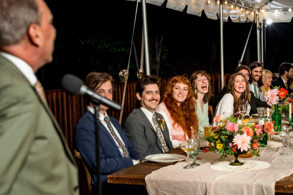 couple sitting at table with bridal party while guests give speeches