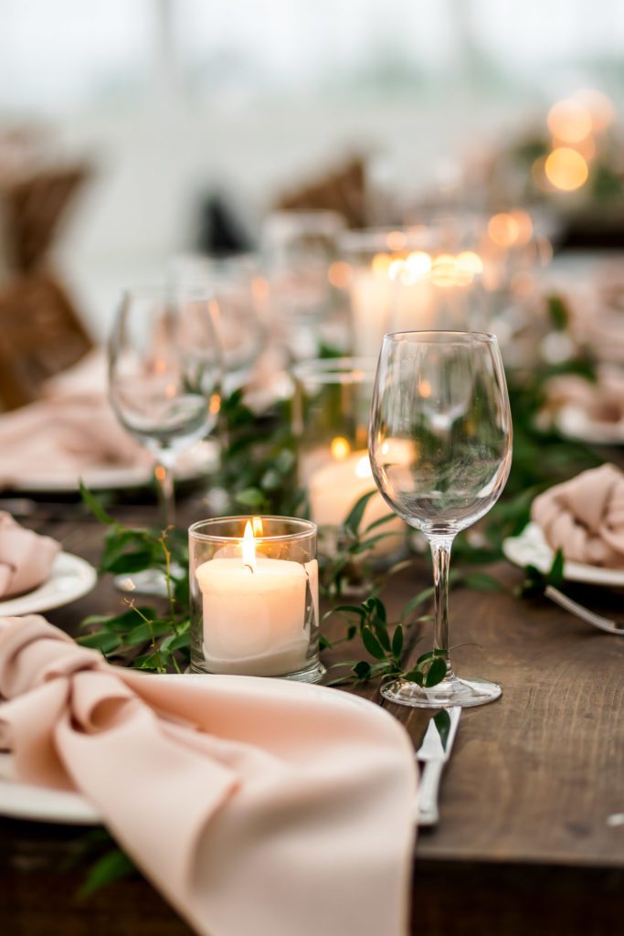 close up of wine glasses alongside blush napkins, candles and greenery on wedding table decor