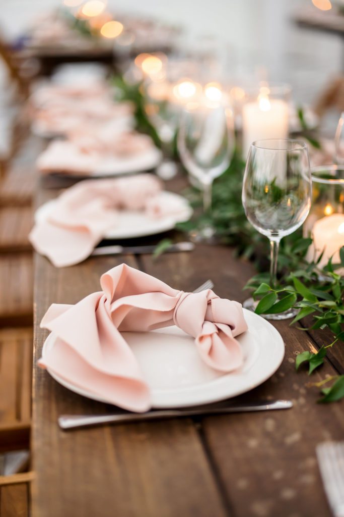 white plates with blush napkins on top of wooden table for wedding table decor