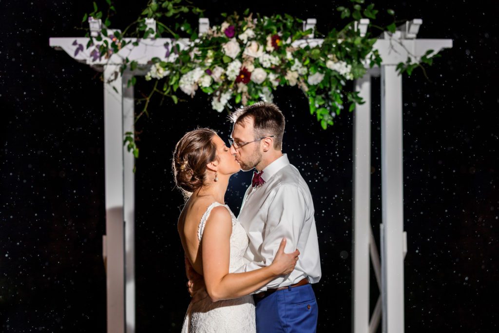 bride and groom kissing under alter during the rain